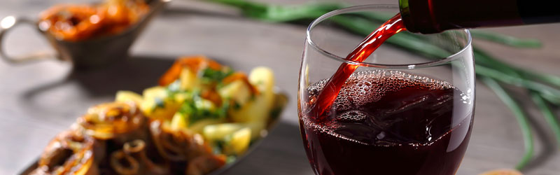 Roter Wein wird in Weinglas auf gedecktem Tisch eingeschenkt